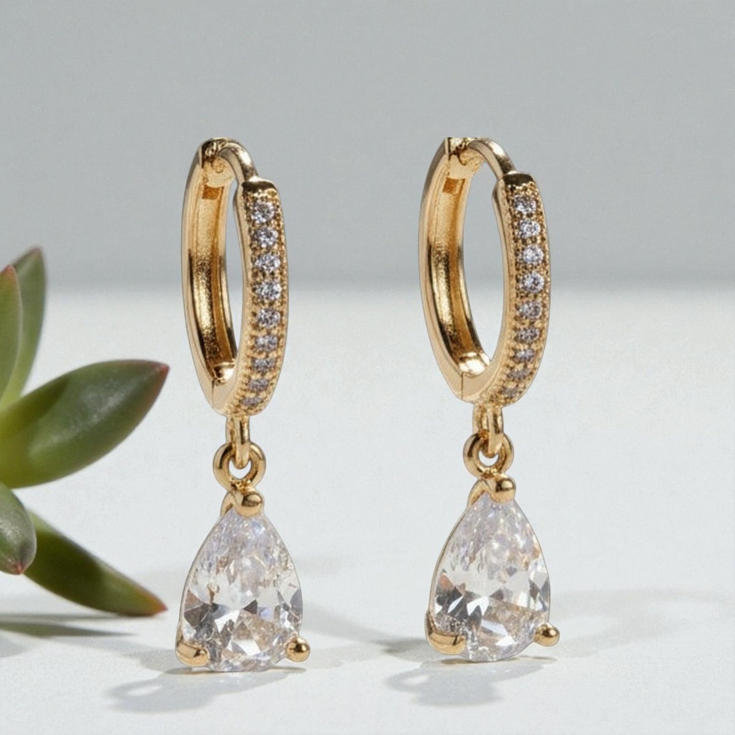 Gold hoop earrings with teardrop-shaped crystals on a light gray background