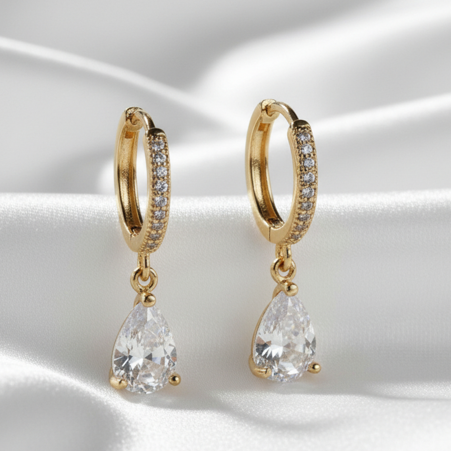 Gold hoop earrings with teardrop-shaped crystals on a satin surface