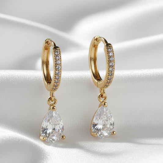 Gold hoop earrings with teardrop-shaped crystals on a satin surface