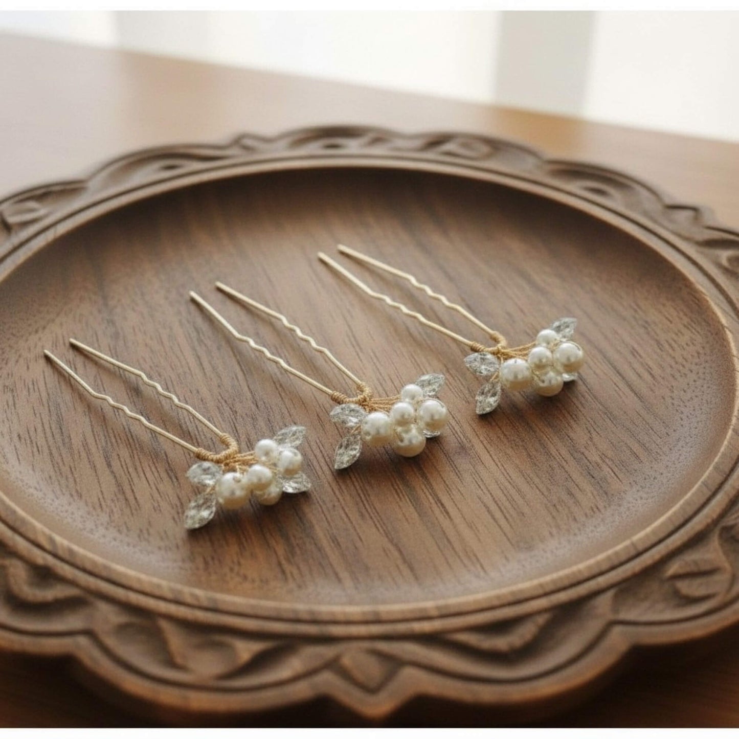 Set of four pearl bridal hair pins arranged on ivory satin fabric, minimal soft‑luxury product flatlay.