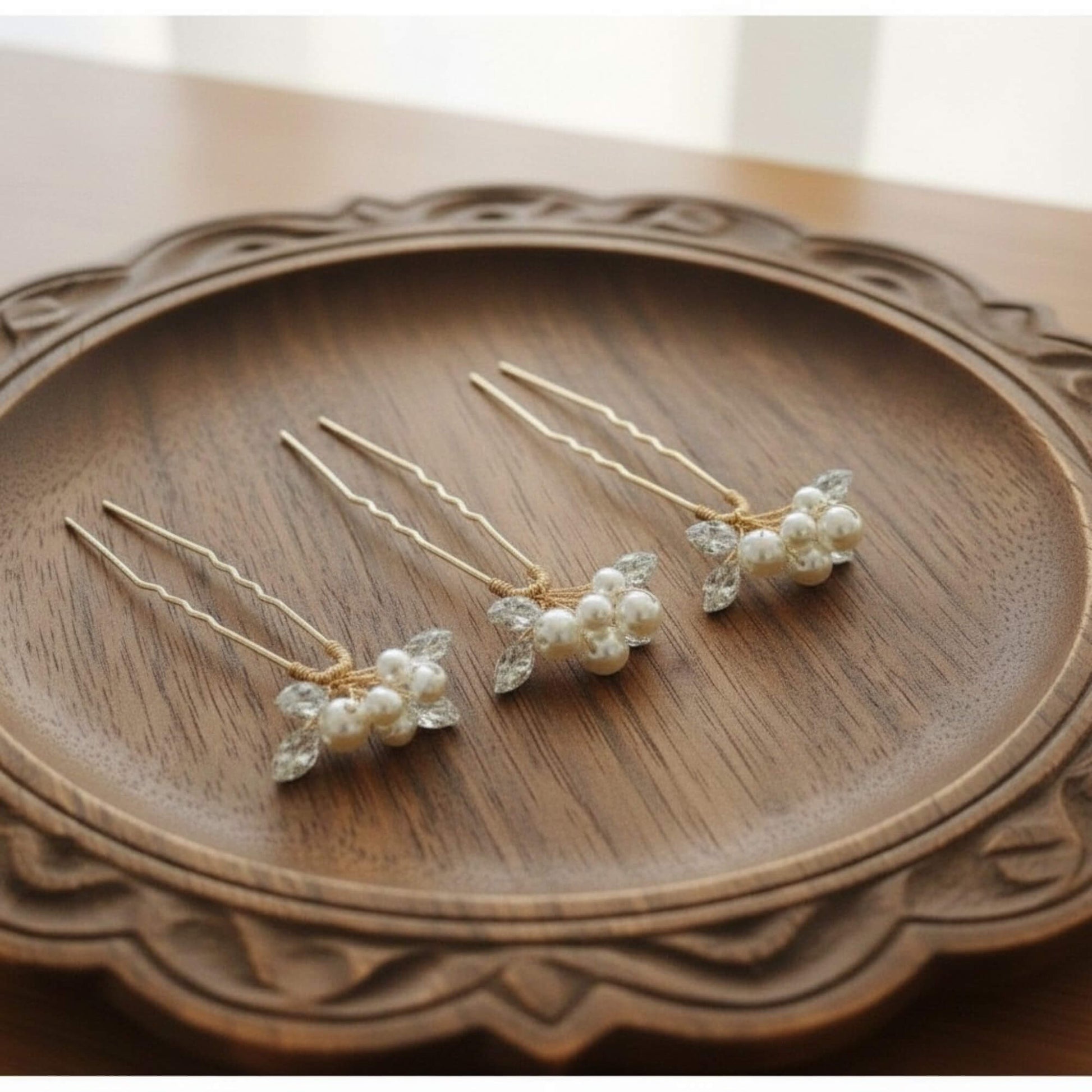Set of four pearl bridal hair pins arranged on ivory satin fabric, minimal soft‑luxury product flatlay.