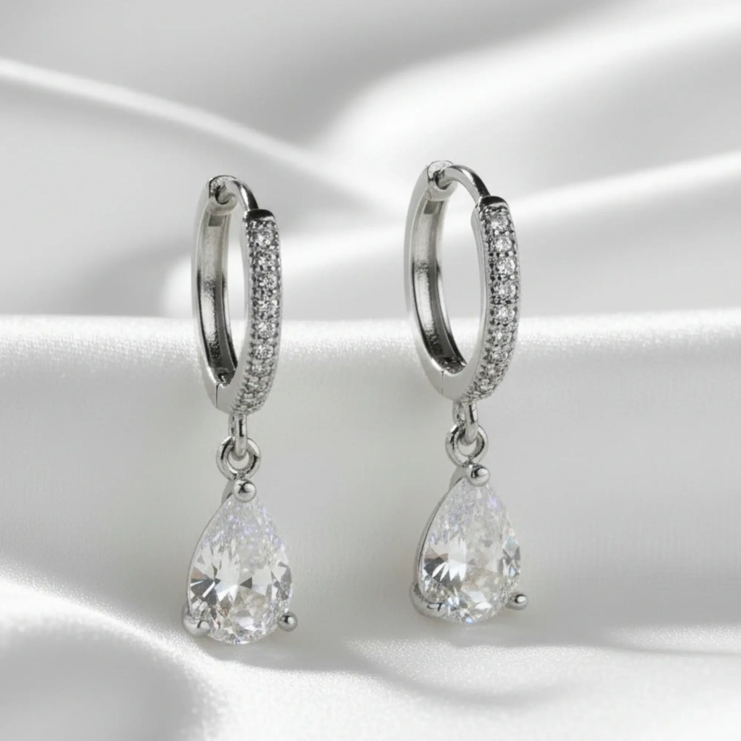 Silver hoop earrings with teardrop-shaped gemstones on a satin surface