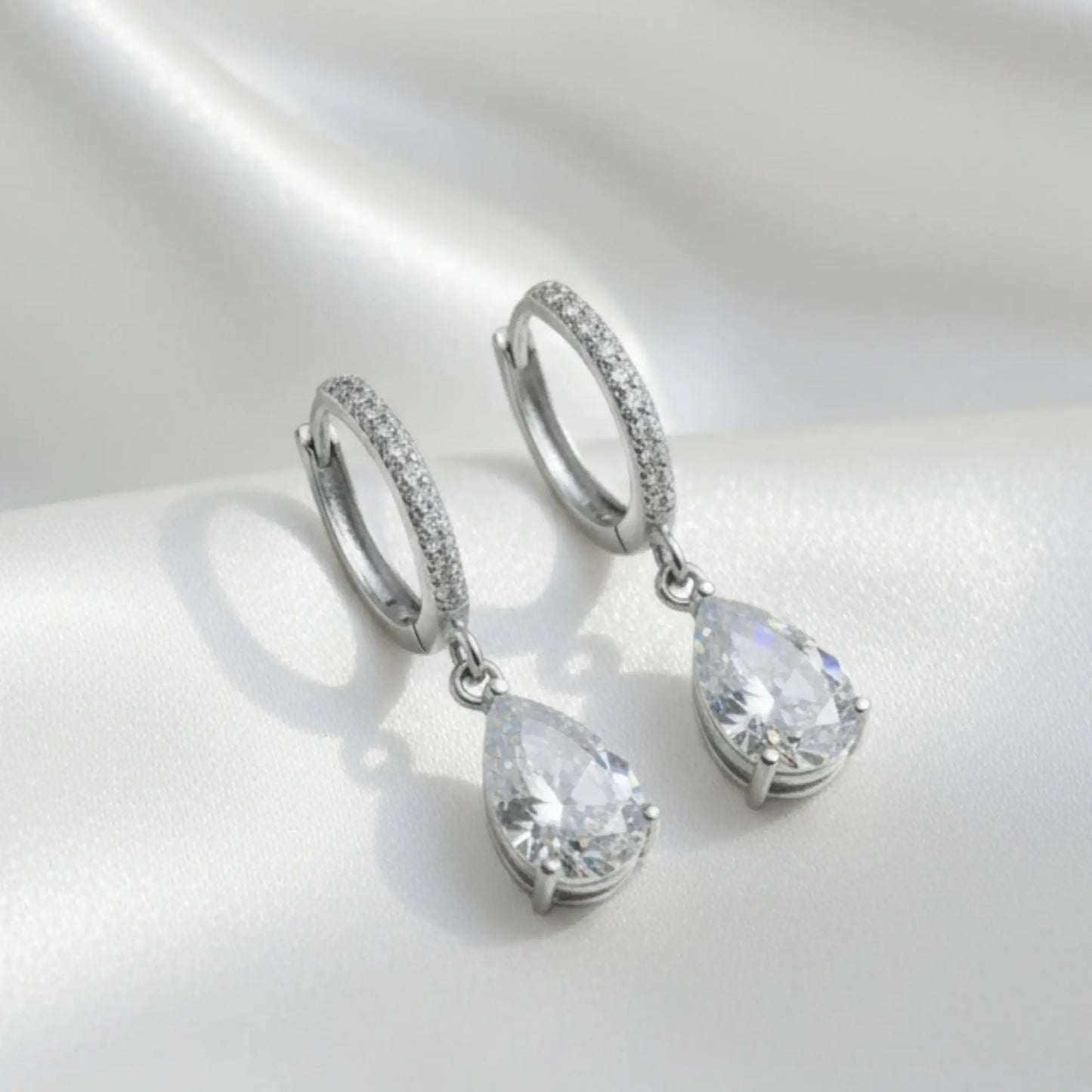 Pair of silver teardrop earrings with clear gemstones on a light gray background