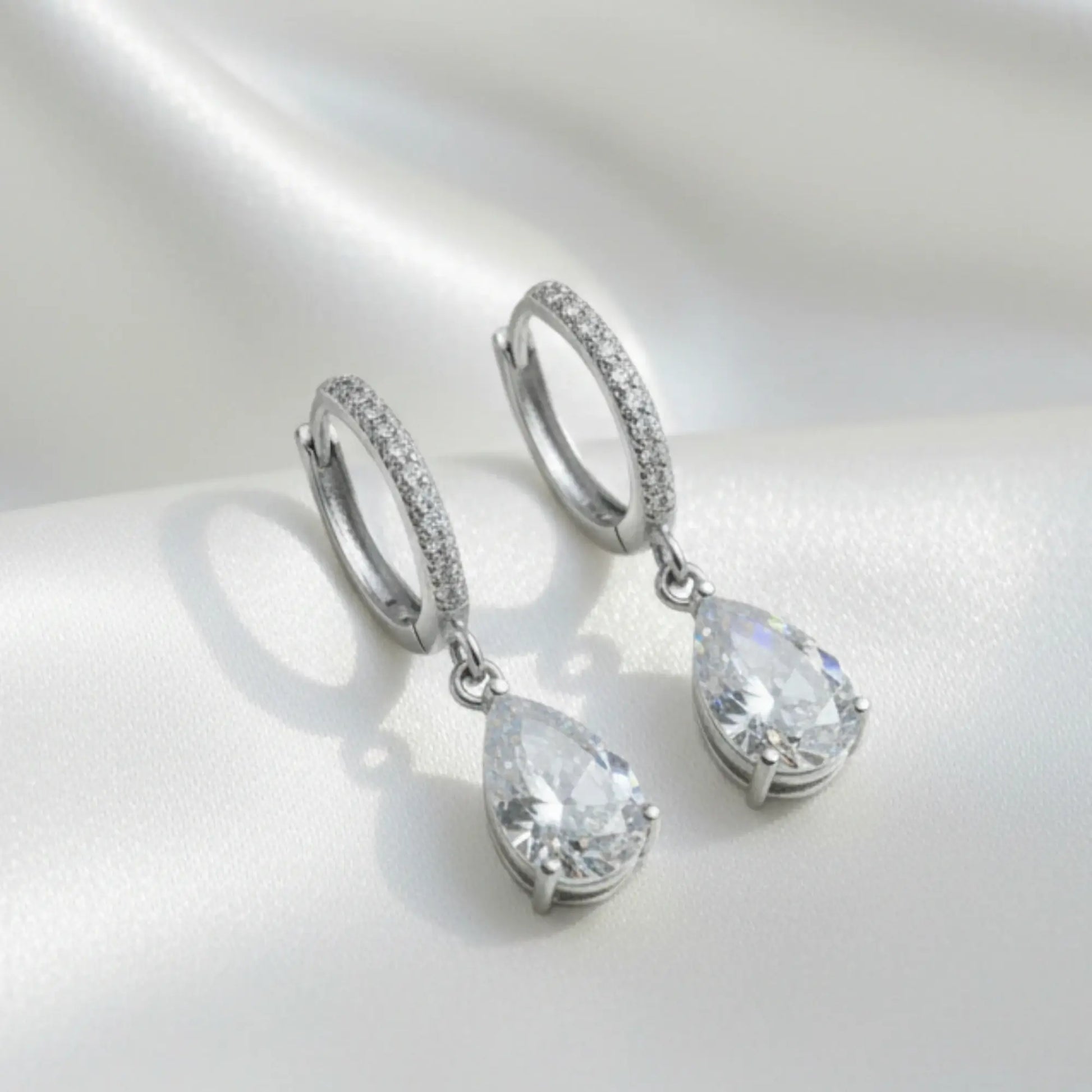 Pair of silver teardrop earrings with clear gemstones on a light gray background
