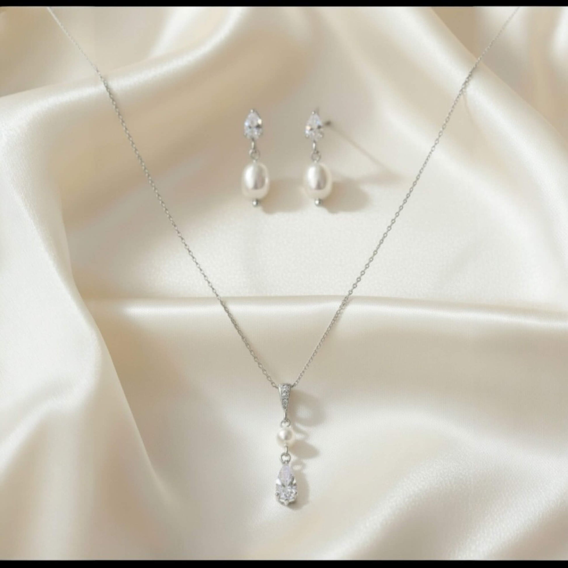 Silver necklace and earrings on a beige fabric background