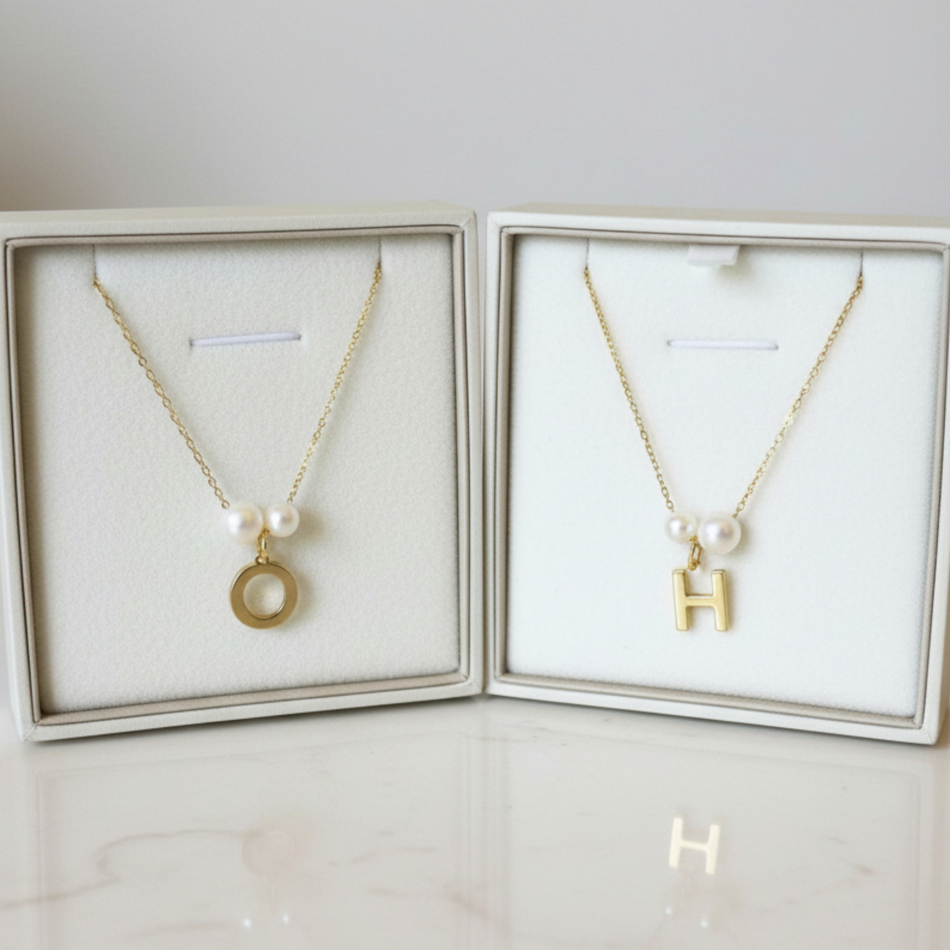 Two gold necklaces with pendants in display cases on a marble surface.