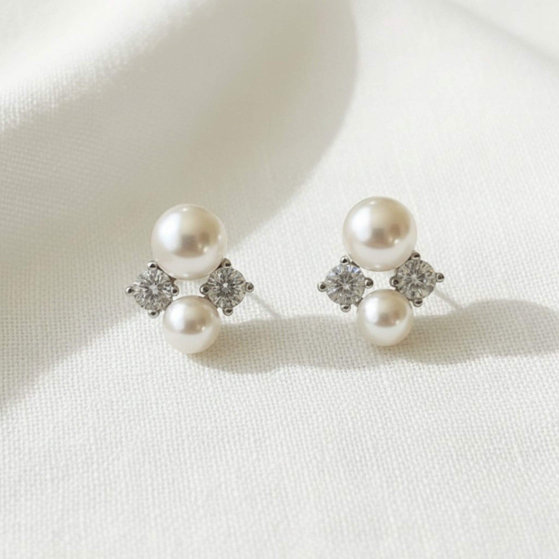 Pearl and zirconia stud earrings on soft white fabric, sterling silver design.