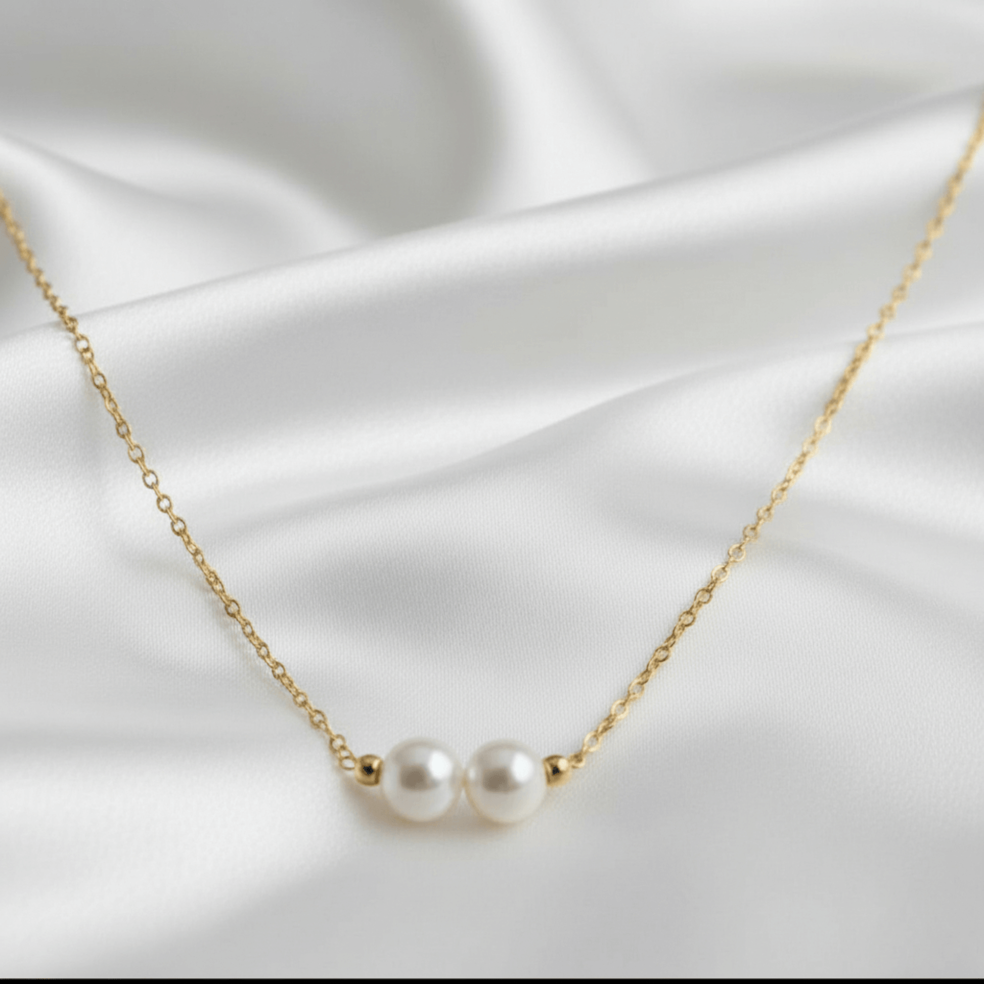 Gold necklace with two pearls on a white satin background