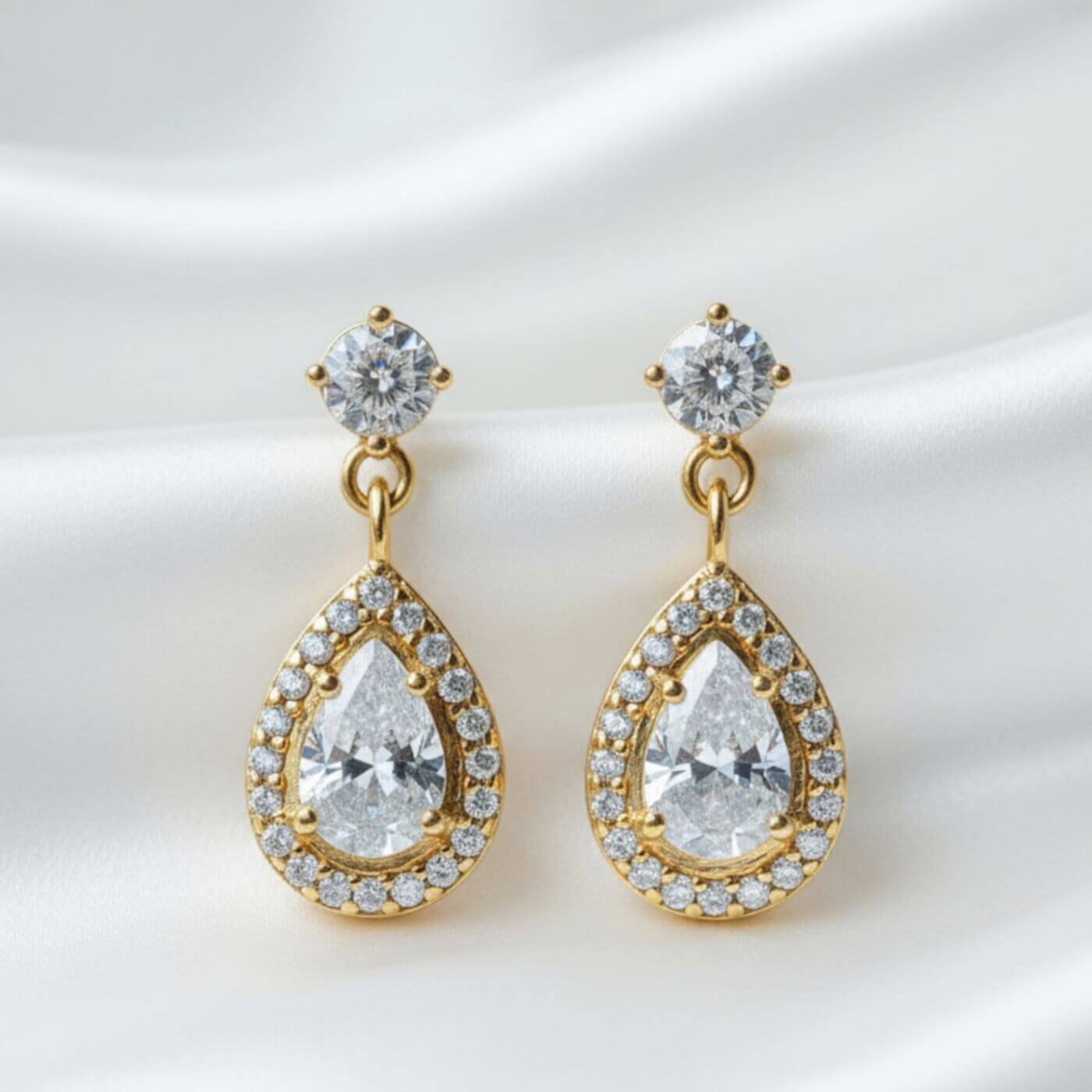 Gold teardrop earrings with clear gemstones on a white background