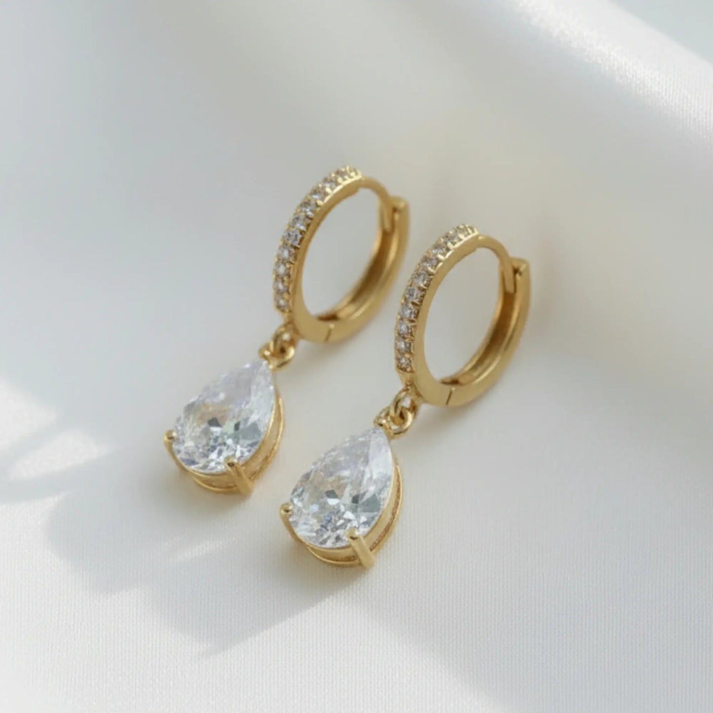 Gold hoop earrings with teardrop-shaped gemstones on a white background