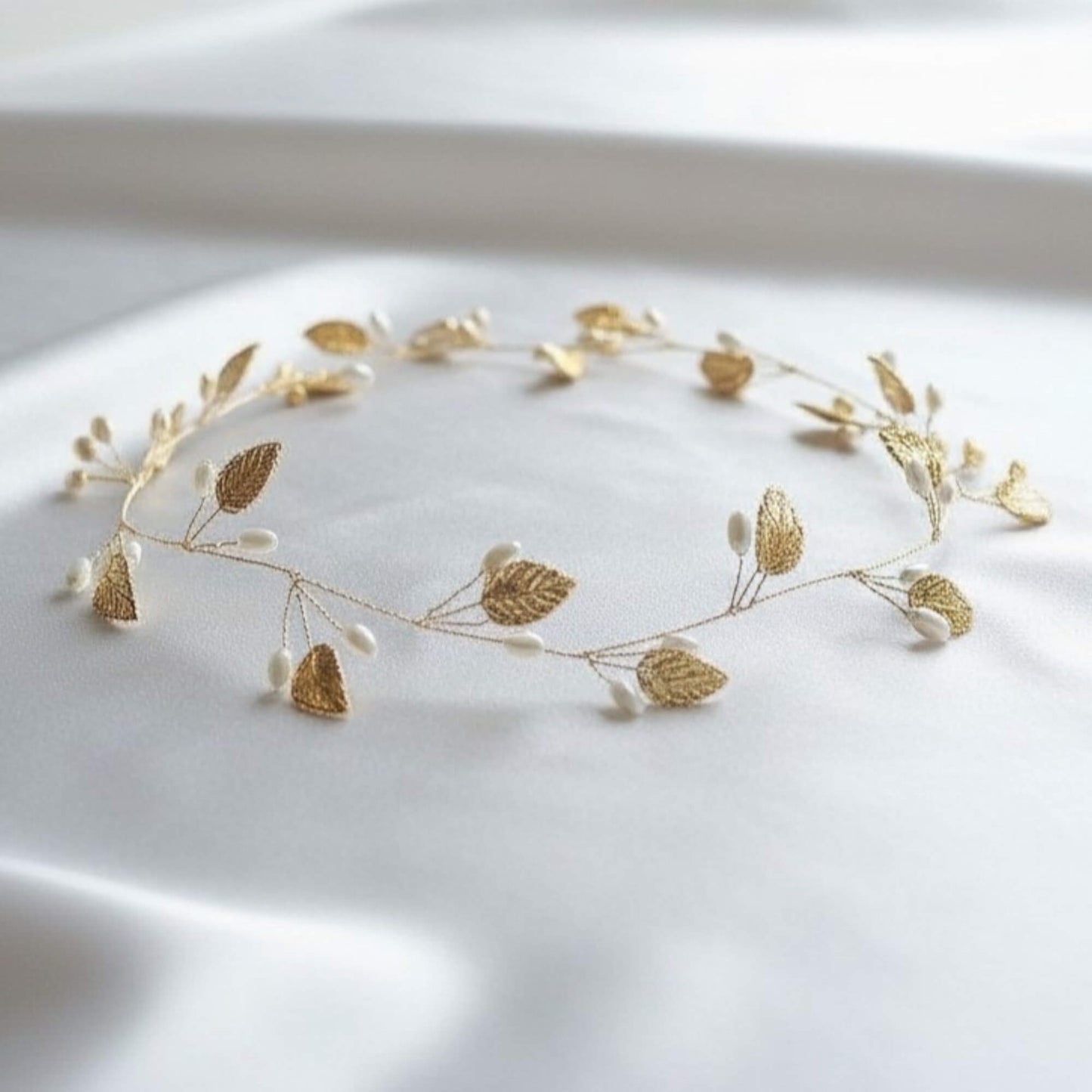 gold pearl leaf bridal hair vine displayed on white satin fabric