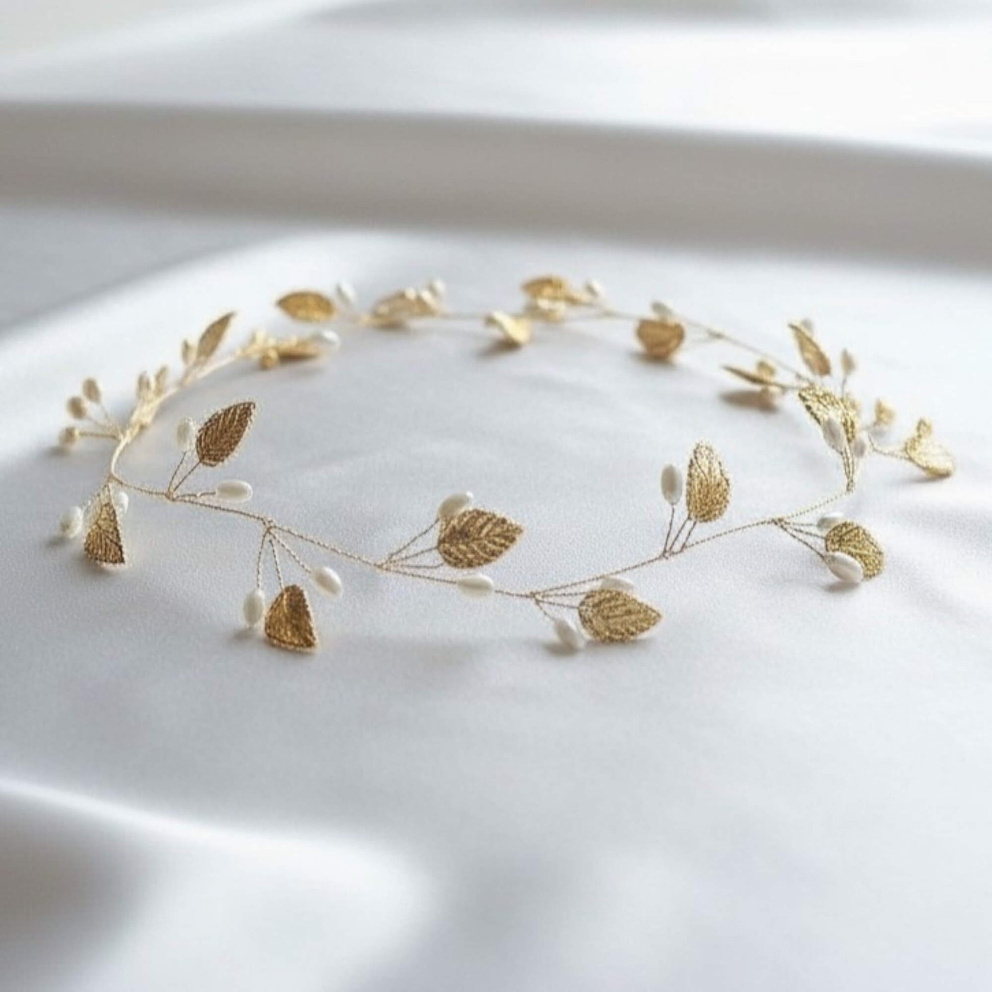 gold pearl leaf bridal hair vine displayed on white satin fabric
