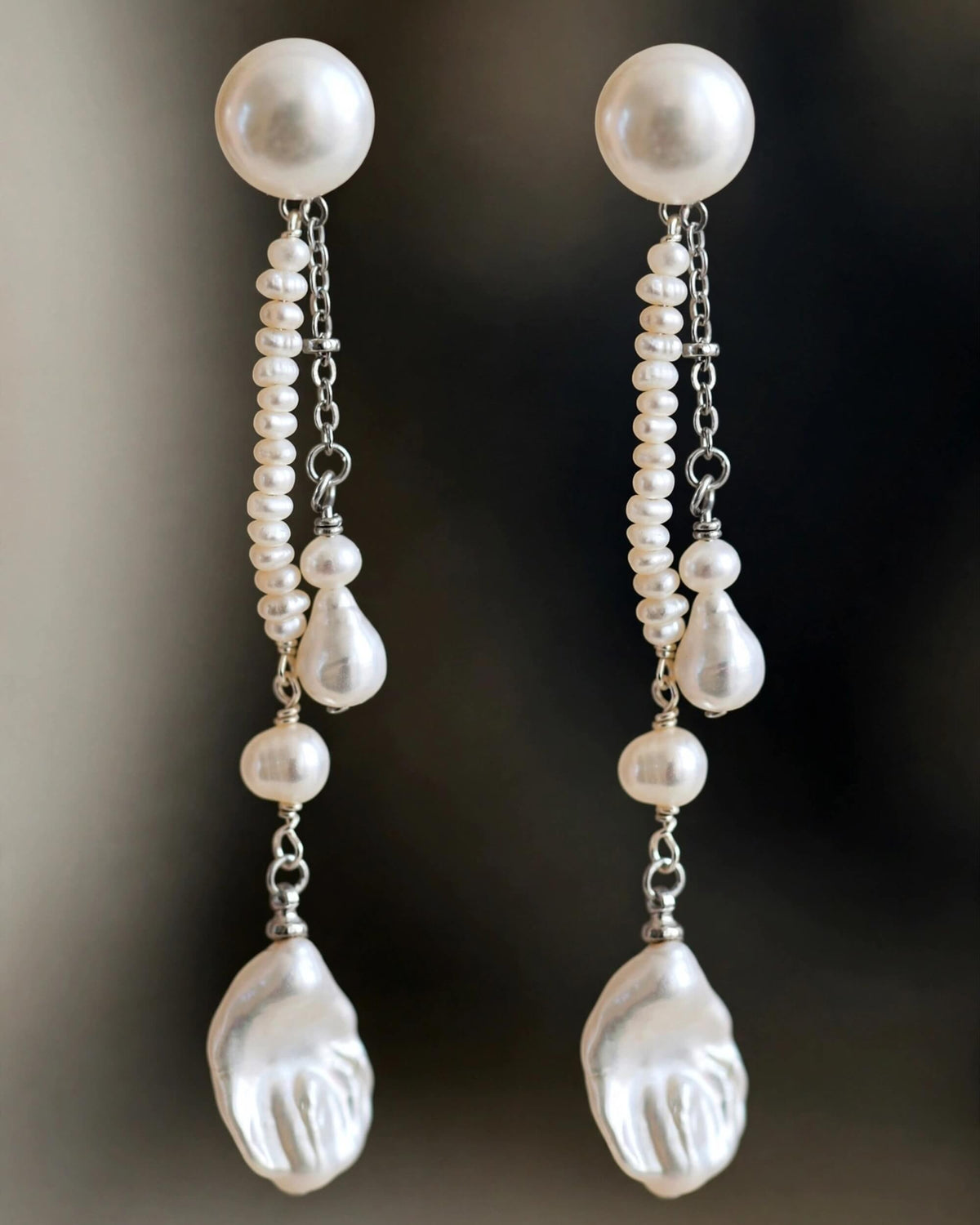 A pair of long drop earrings featuring large white freshwater pearls and smaller white baroque pearls suspended from silver chains, with teardrop-shaped white pearl charms at the bottom.