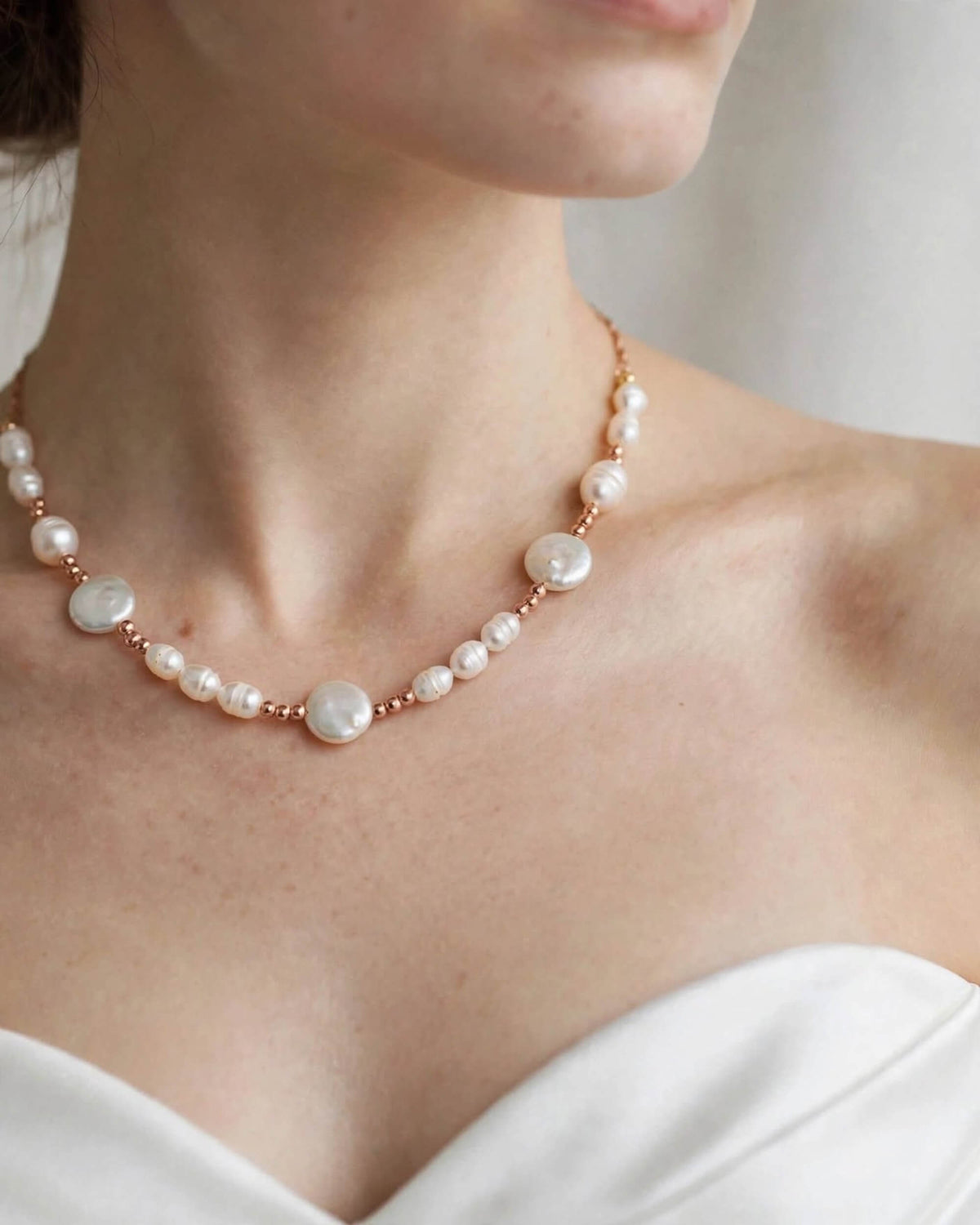 A close-up of a woman's neck and upper chest wearing a delicate necklace made of white pearls and rose gold beads.