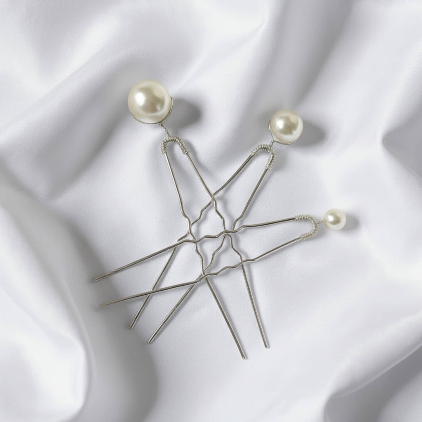 Flatlay of three gold pearl hairpins arranged on soft white fabric