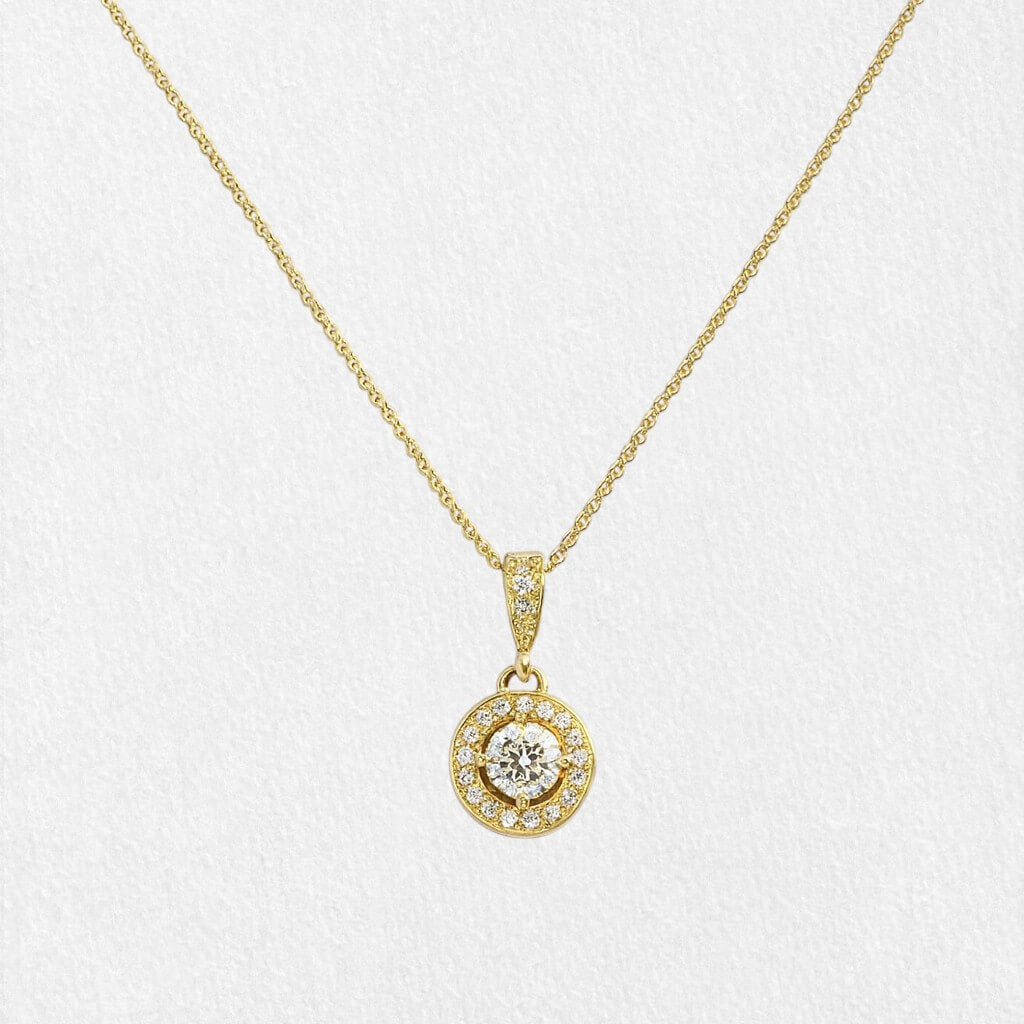 Gold halo pendant necklace held gently by bride’s hand, showcasing central diamond and fine craftsmanship