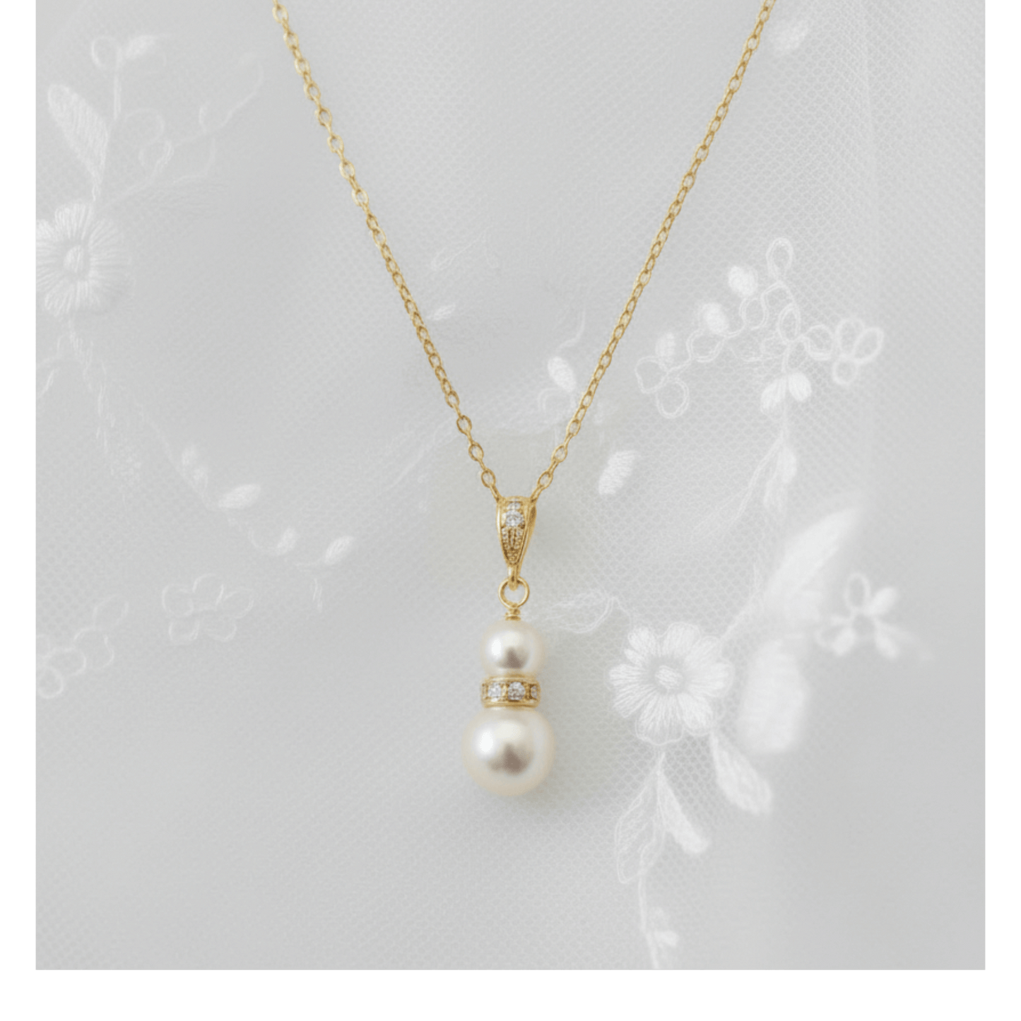 Gold and pearl pendant necklace photographed on embroidered lace background