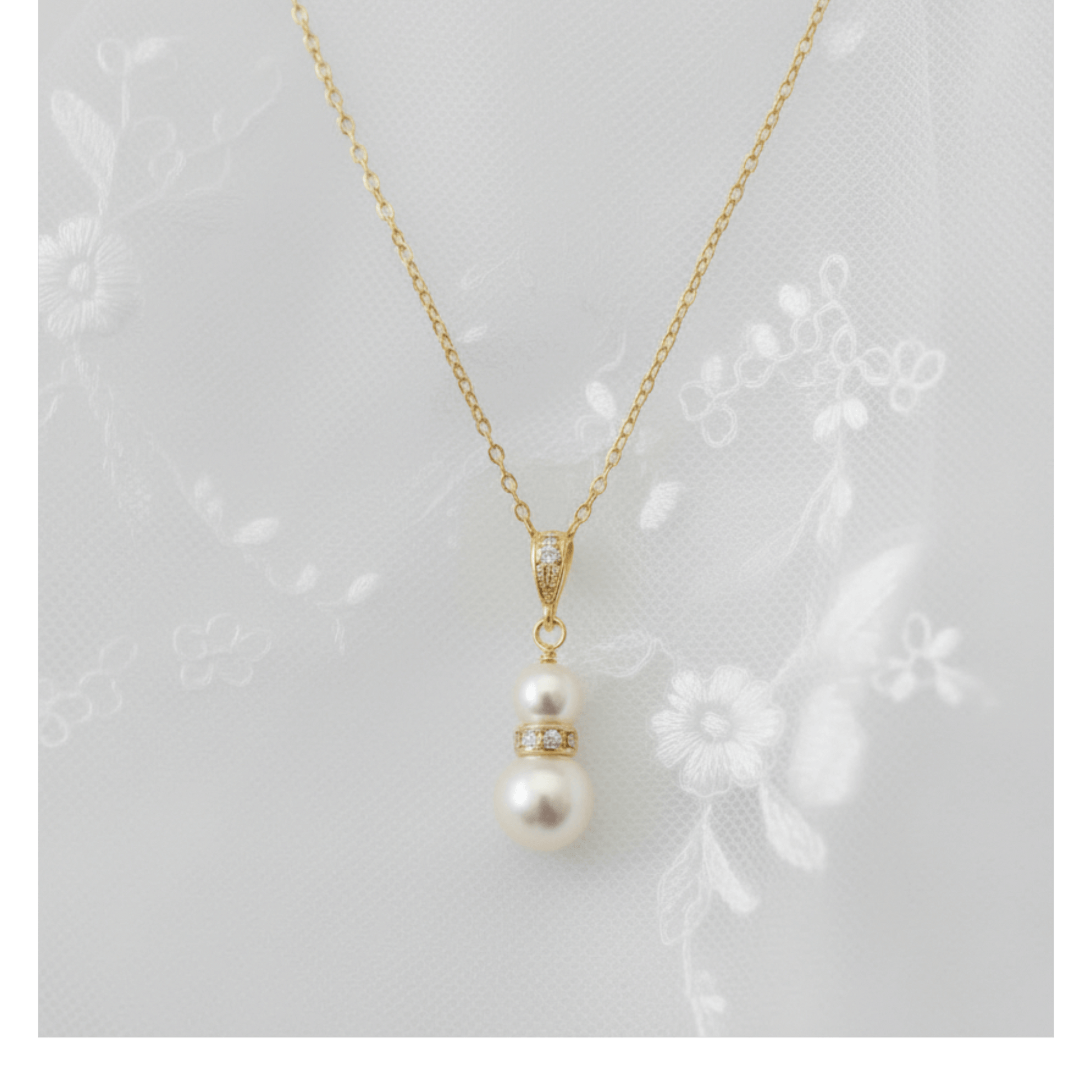 Gold and pearl pendant necklace photographed on embroidered lace background