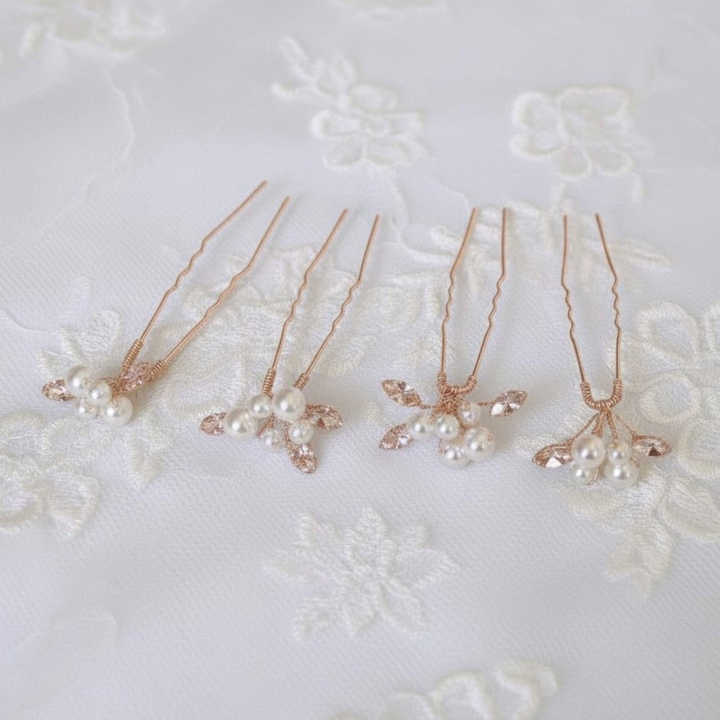 Four handcrafted pearl hair pins displayed on champagne satin, showing clean details and elegant bridal styling.