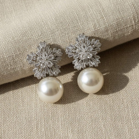 Pearl drop earrings with crystal cluster top on soft ivory background.