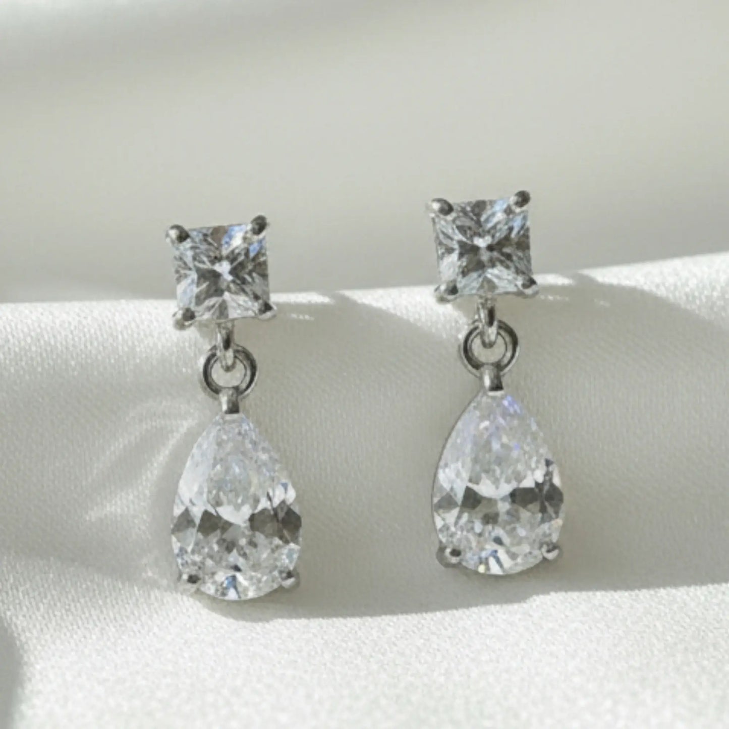 Pair of silver earrings with clear gemstones on a white background