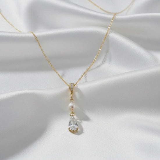 Close‑up video of a teardrop pearl pendant necklace in 925 sterling silver, showing the freshwater pearl, zirconia crystal and chain details on soft satin