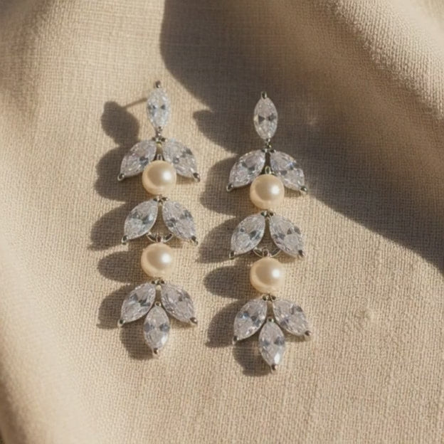 High-end pearl and crystal cluster earrings displayed on soft beige fabric for bridal styling.