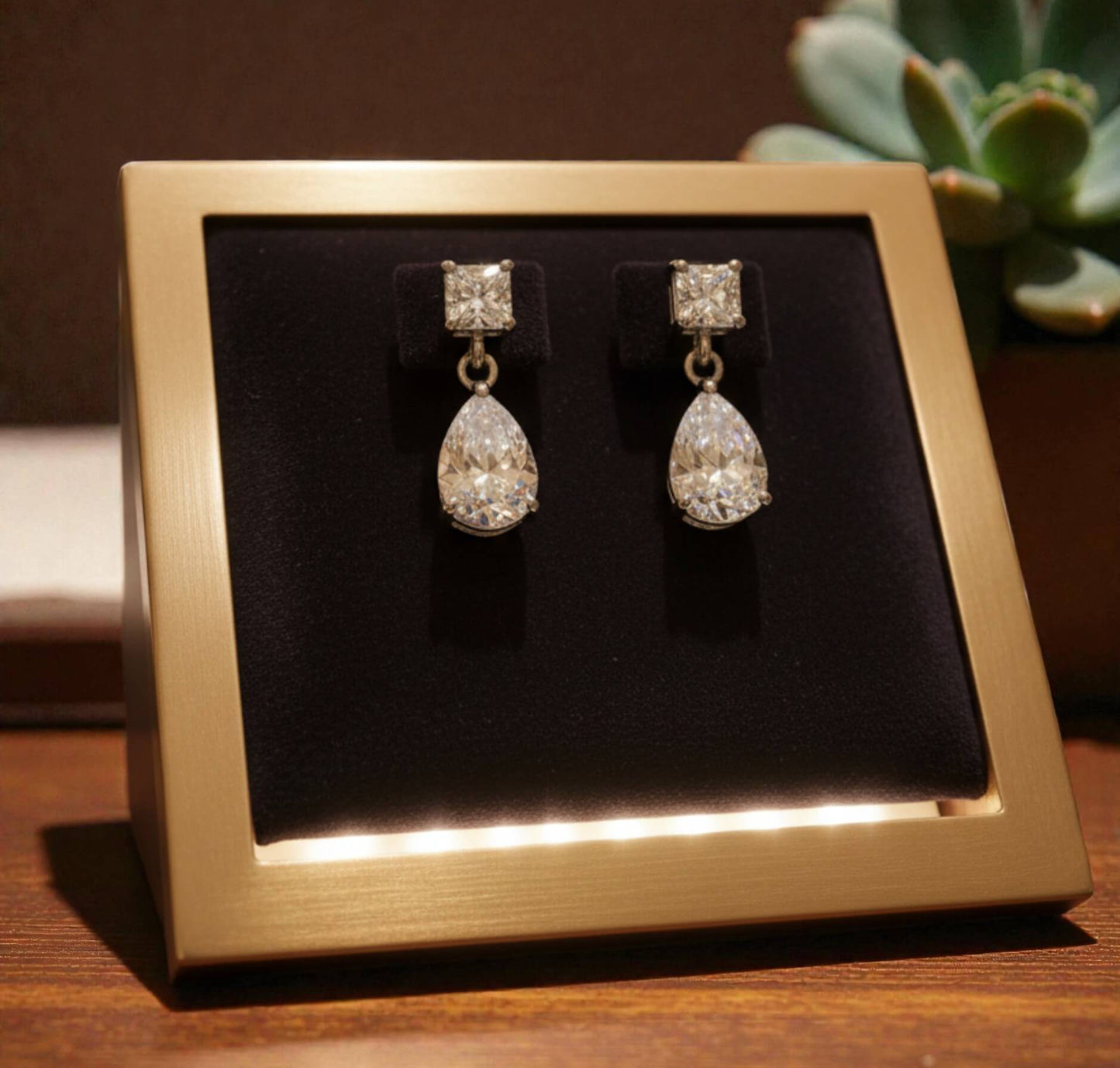 Teardrop-shaped earrings on a black display card with a gold frame, set against a blurred background.