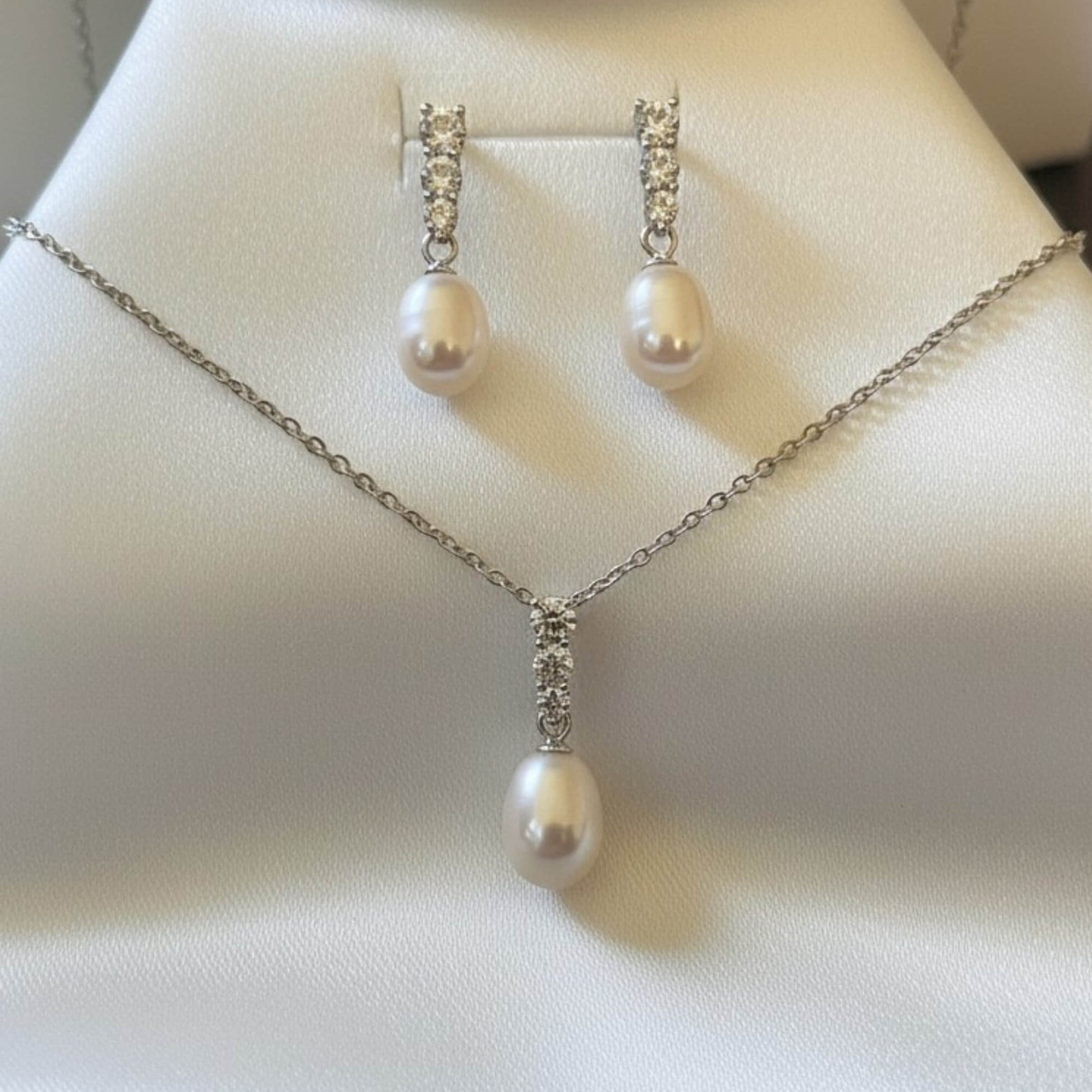 Elegant teardrop freshwater pearl necklace and earrings set in 925 silver displayed on white satin.