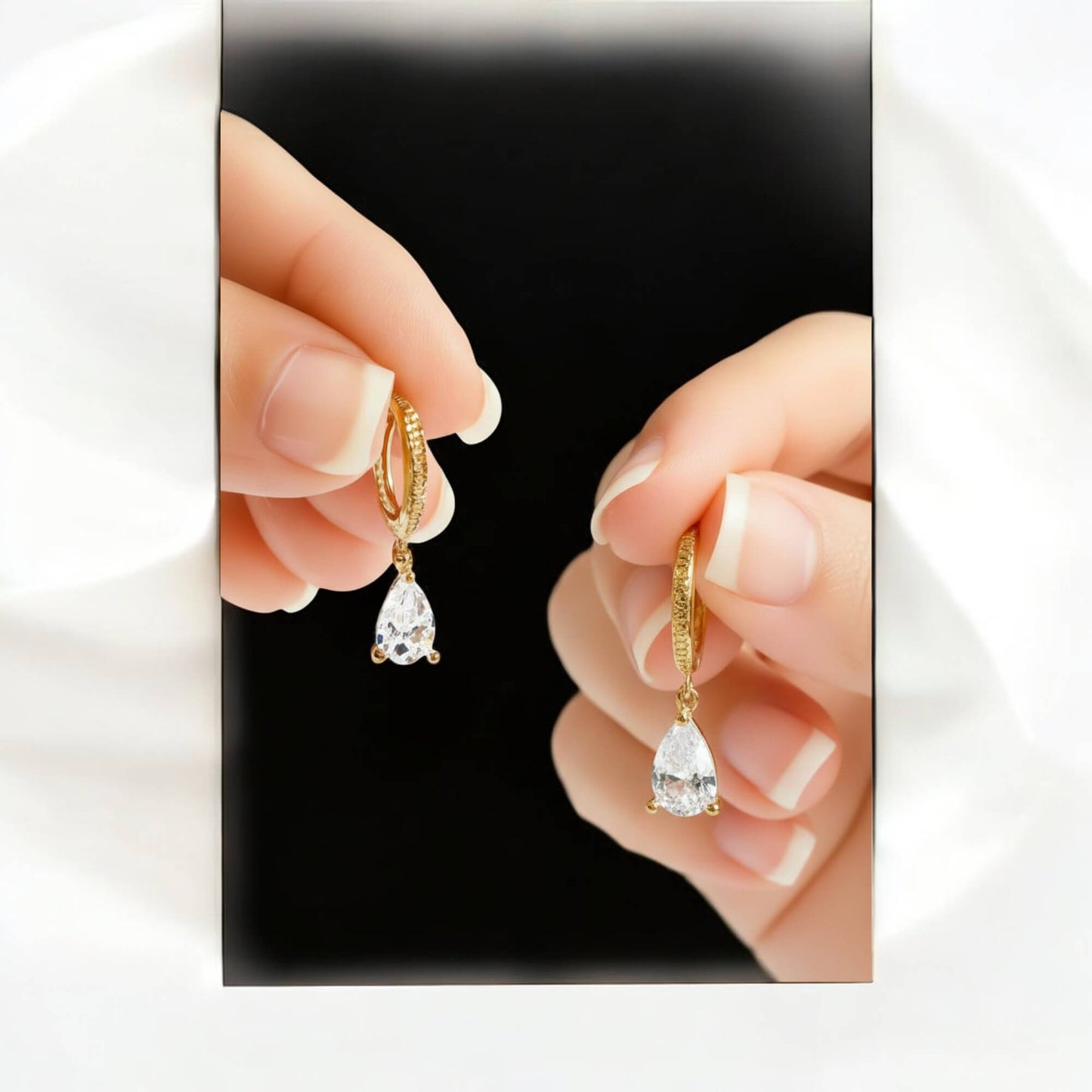 Gold earrings with clear gemstones held between fingers against a black background