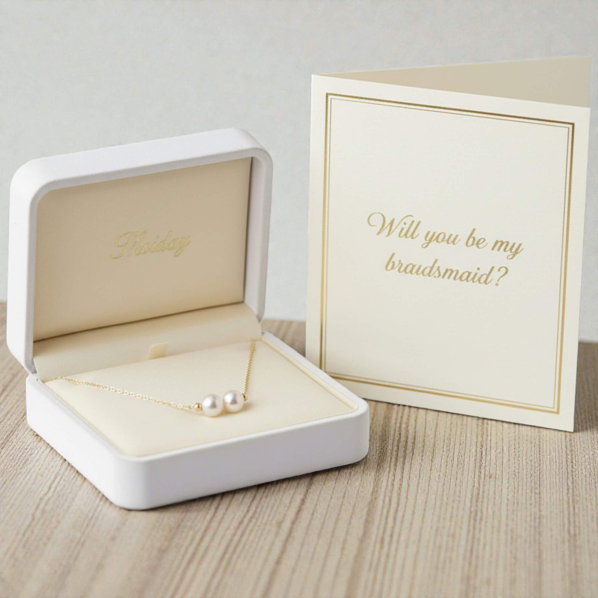 Pearl necklace in a box with a 'Will you be my bridesmaid?' card on a wooden surface.